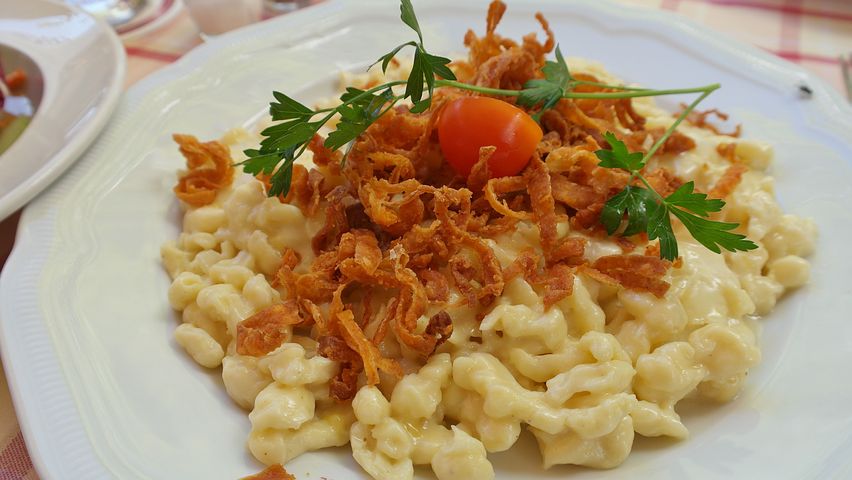 A classic German meal of spätzle a creamy pasta topped with fried onions, and a garnish consisting of parsley and a cherry tomato